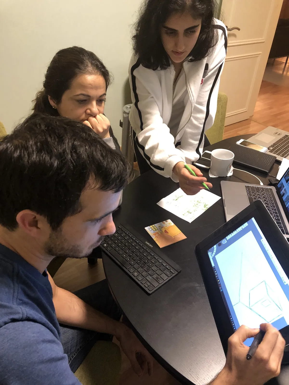 Three team members at work around a table with pen tablets and keyboards.