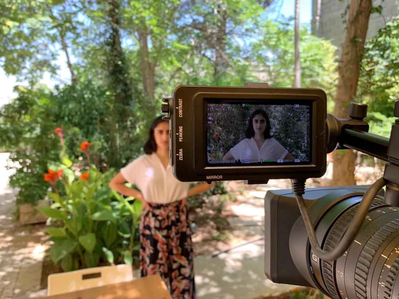 On location in a garden: a camera monitor frames a woman standing among the plants.