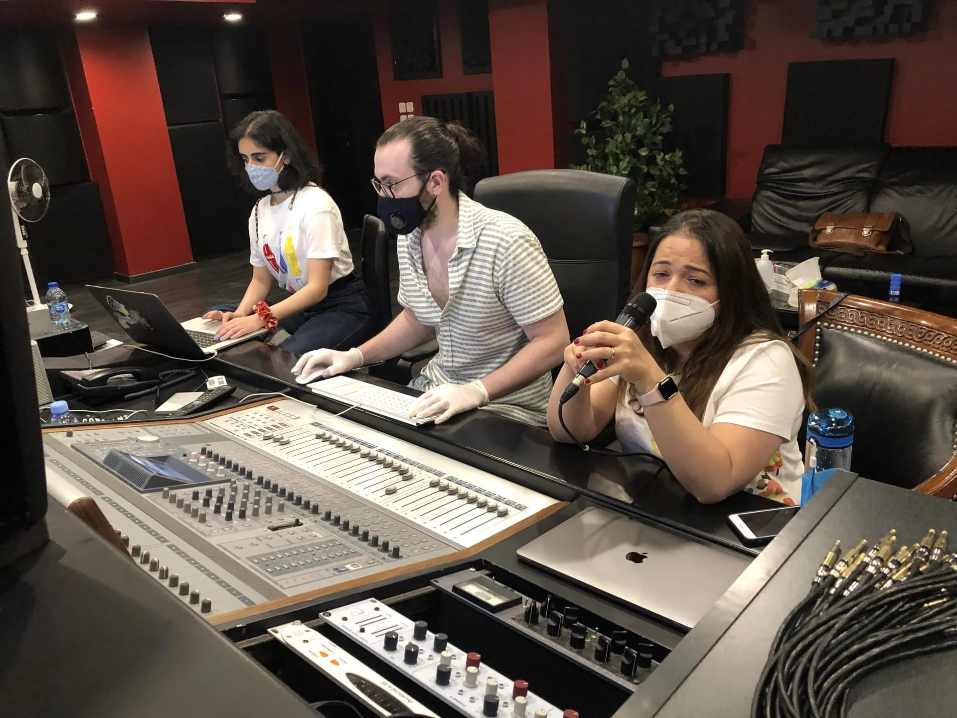 The team at a large mixing console in a sound studio, one of them speaking into a microphone.