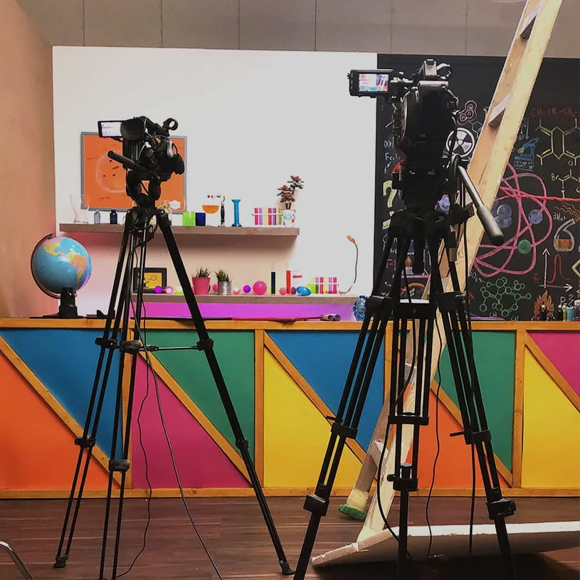Two cameras facing a brightly painted studio set.